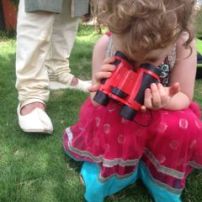 T using her binoculars to search for worms and lizards at the wedding ceremony (A's feet in background).